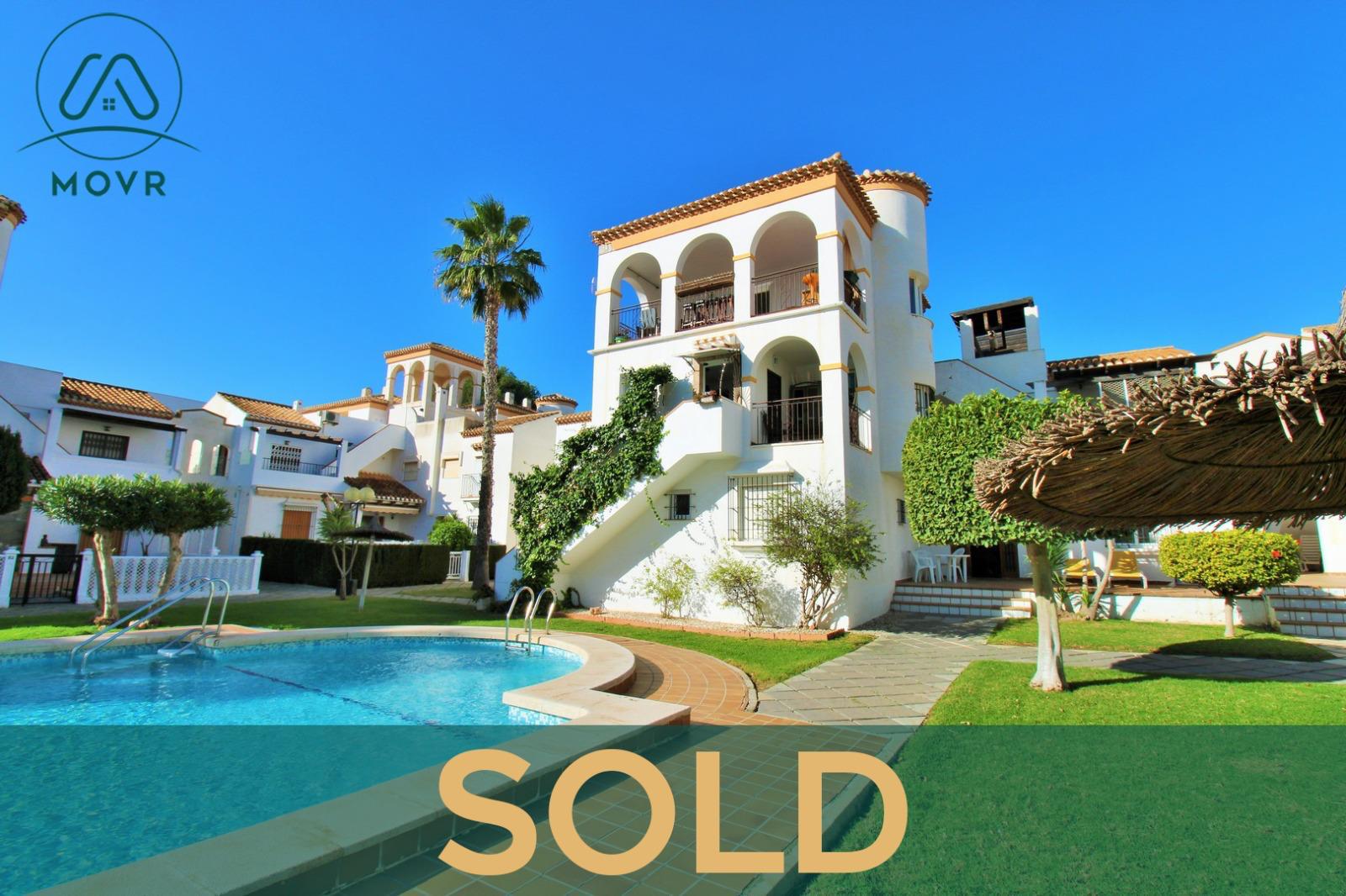 Whitewashed apartment block beside a garden pool previously sold by MOVR in Orihuela Costa